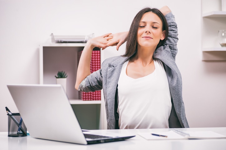 Young businesswoman is relaxing in her office. She is stretching her body.