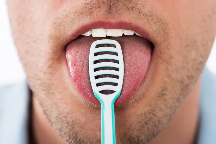 Close-up Of Young Man Cleaning His Tongue With Scraper