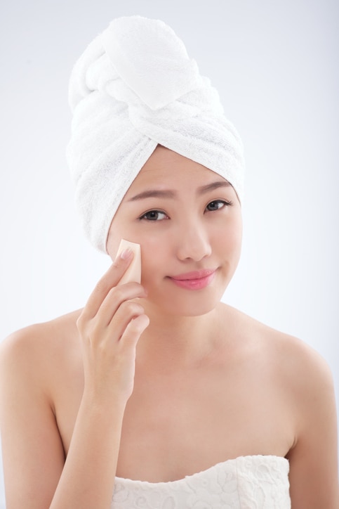 Attractive young woman applying foundation with sponge