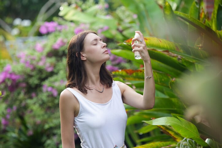 Woman spraying facial mist on her face, summertime skincare concept