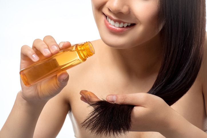 cropped shot of smiling woman pouring oil on split ends isolated on white