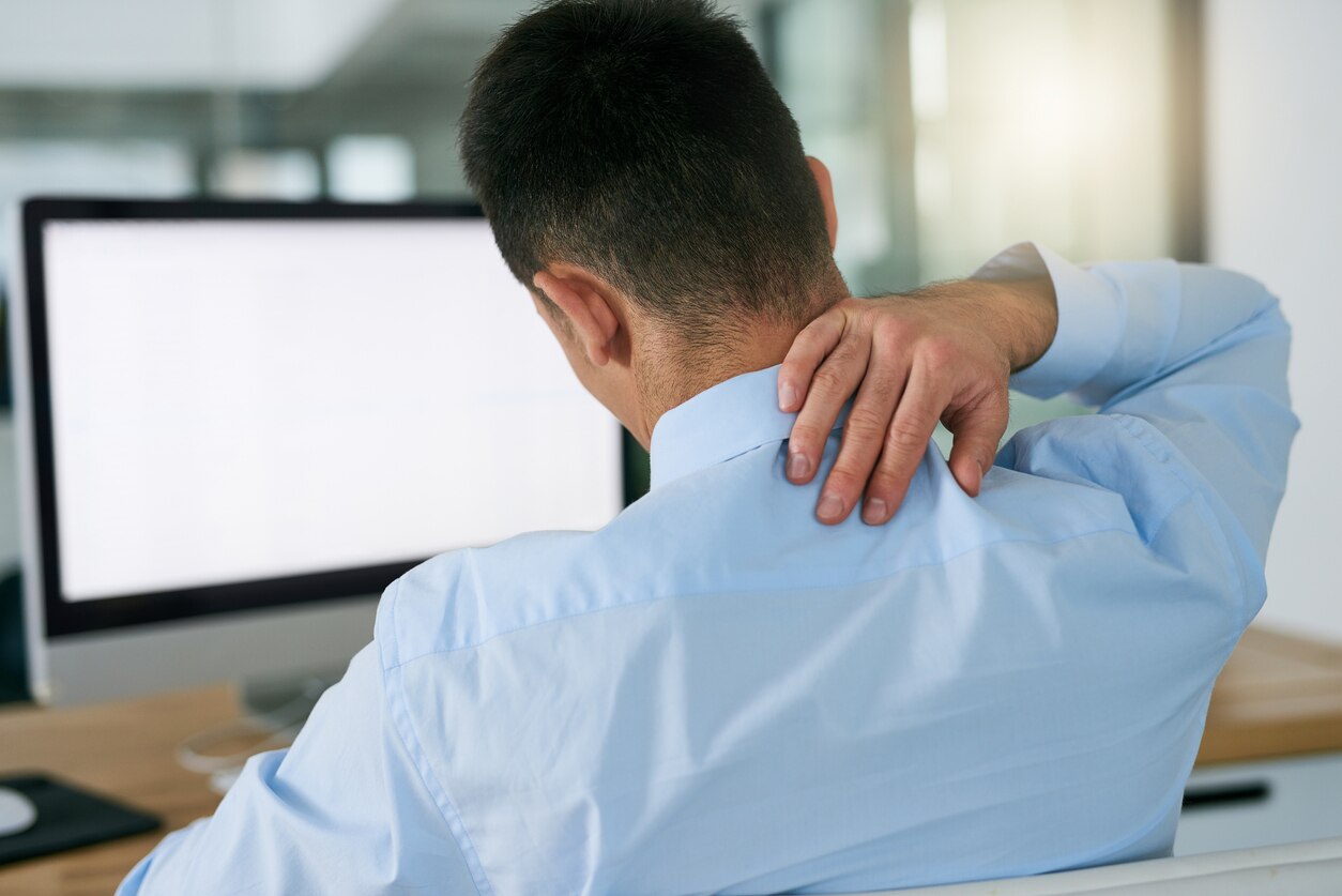 Rearview shot of a young businessman holding his neck while sitting at his desk