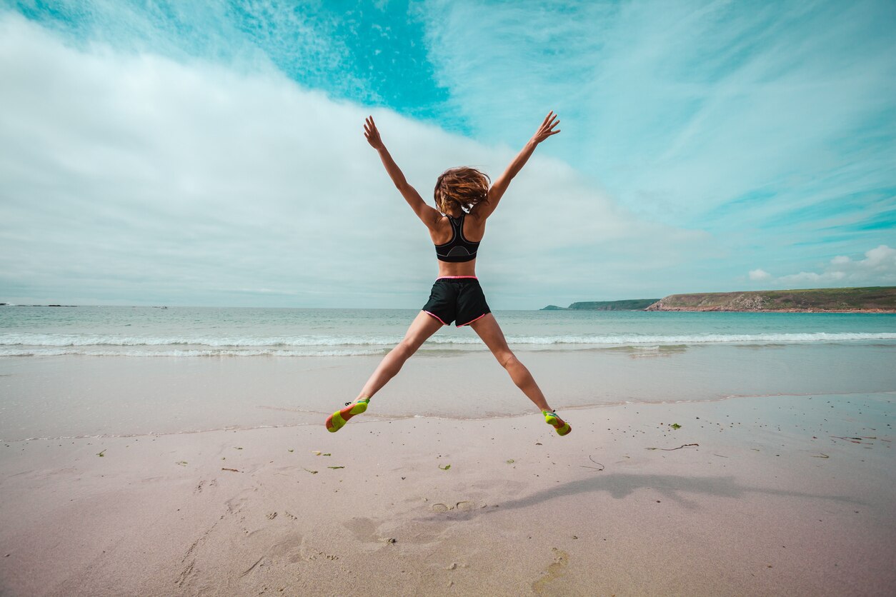 A young woman is doing star jumps on the beach by the sea