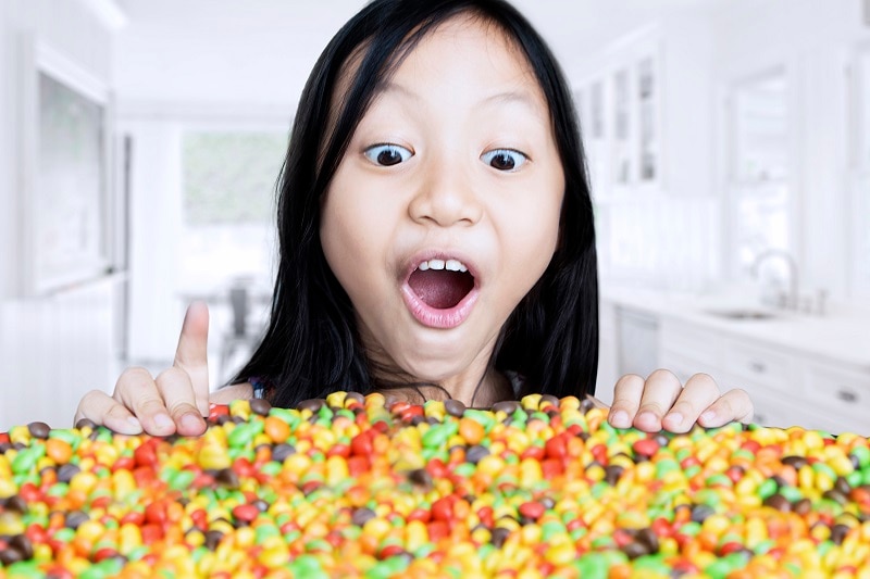 Photo of a surprised little girl looking at colorful candies on the table, shot in the kitchen at home