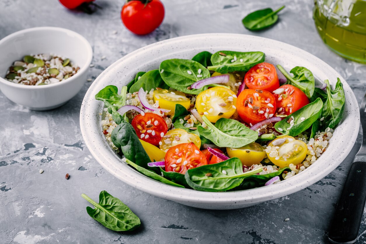 Healthy green bowl salad with spinach, quinoa, yellow and red tomatoes, onions and seeds on gray background