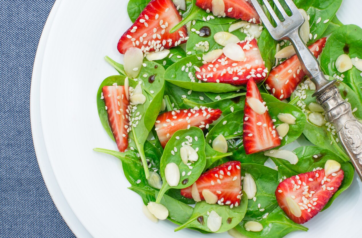 Salad spinach leaves, strawberries, almonds and sesame seeds, top view.Light, healthy, vegan food concept.